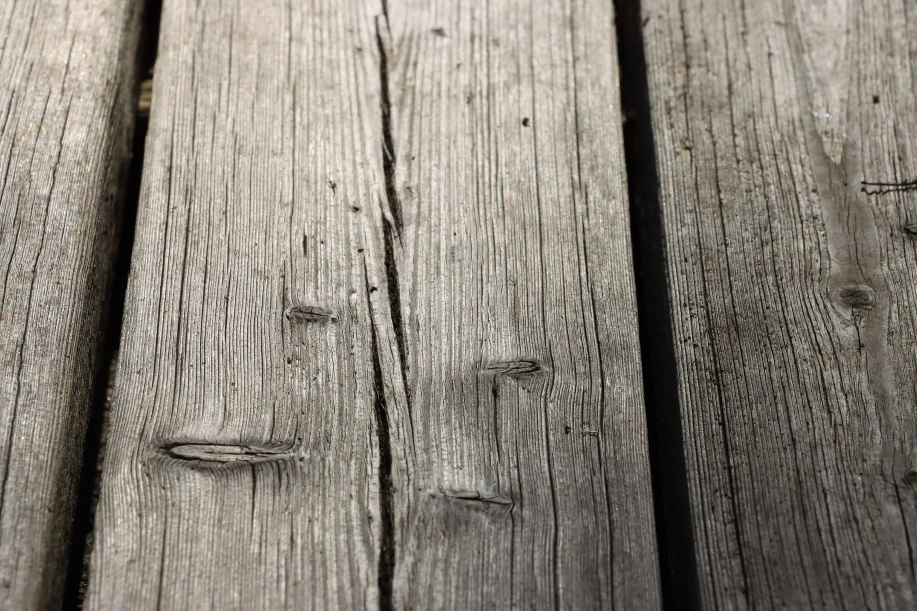 Close view of old gray deck boards with deep cracks, splits, and raised nail heads, Charleston area